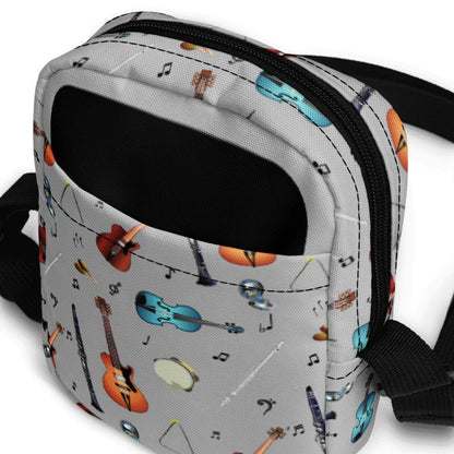Grey crossbody bag with black adjustable shoulder strap (with black plastic clip), inside and outside pockets, sturdy fabric, and two-way zipper. The design features a repeat pattern of colourful musical instruments and black musical notes on a grey background.