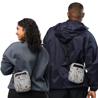Grey crossbody bag with black adjustable shoulder strap (with black plastic clip), inside and outside pockets, sturdy fabric, and two-way zipper. The design features a repeat pattern of colourful musical instruments and black musical notes on a grey background.