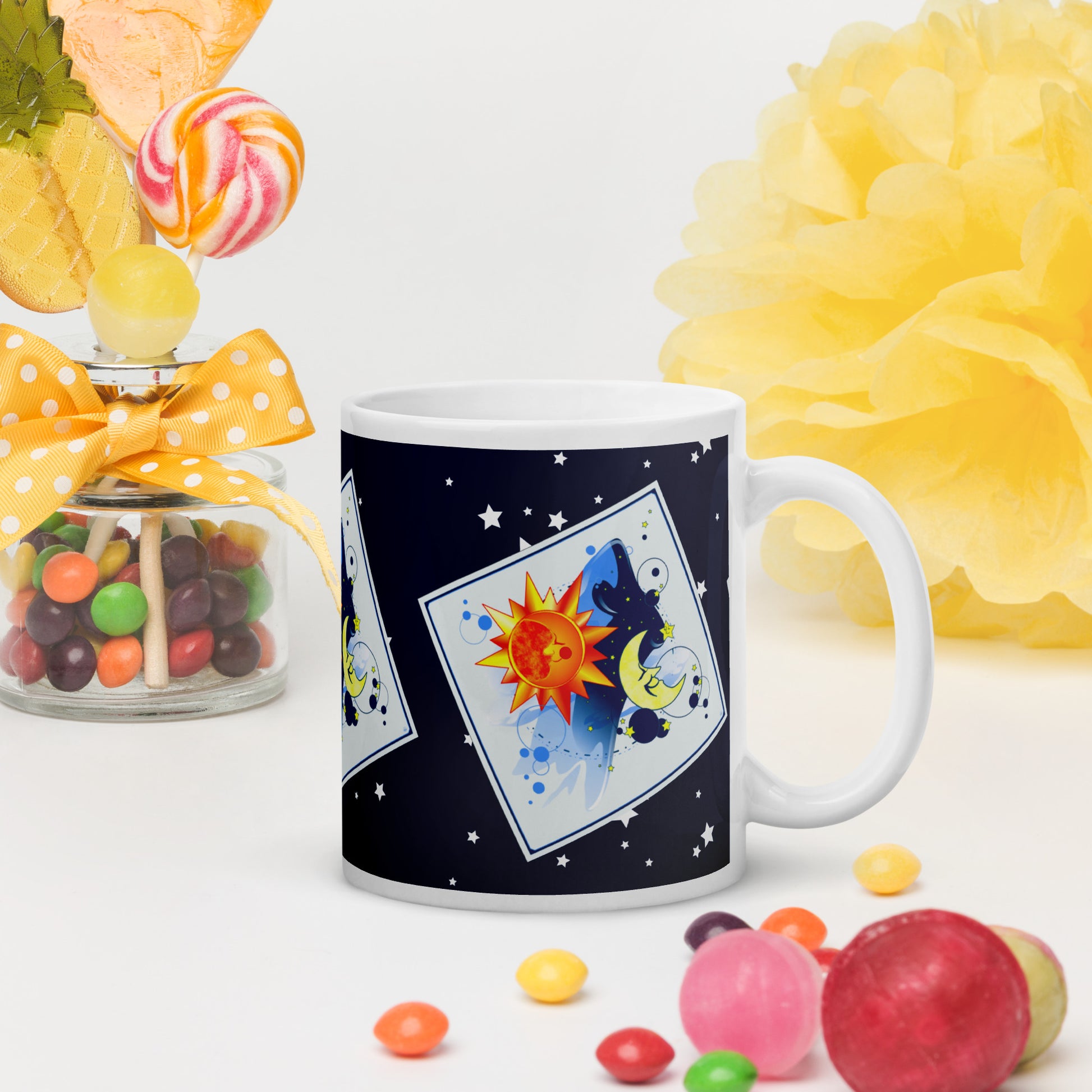 Mug with a sun and moon design on a table surrounded by colourful candies and yellow paper flowers.