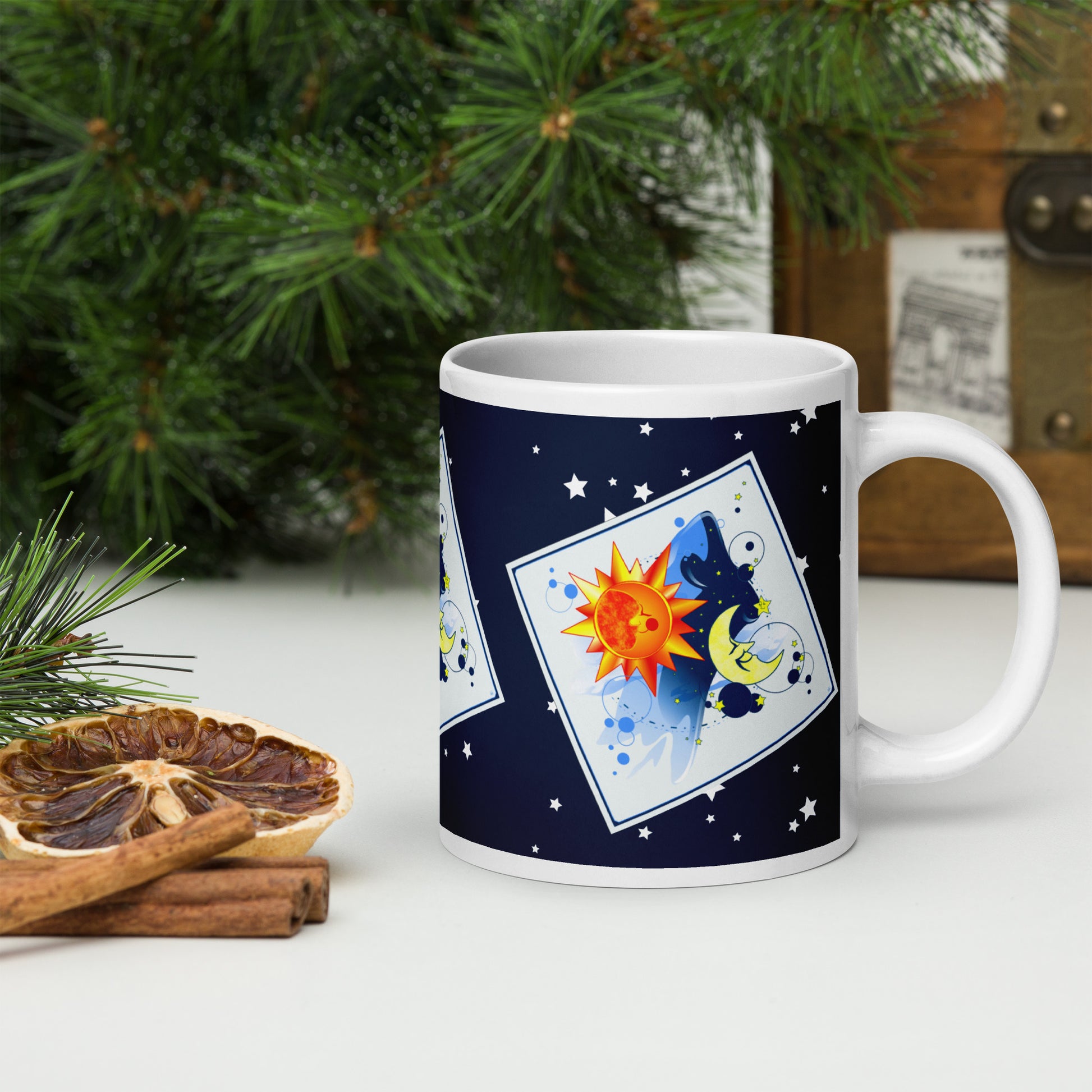 Mug with a sun and moon design on a table with seasonal decorations (pine needle, a dried orange slice and cinnamons sticks).