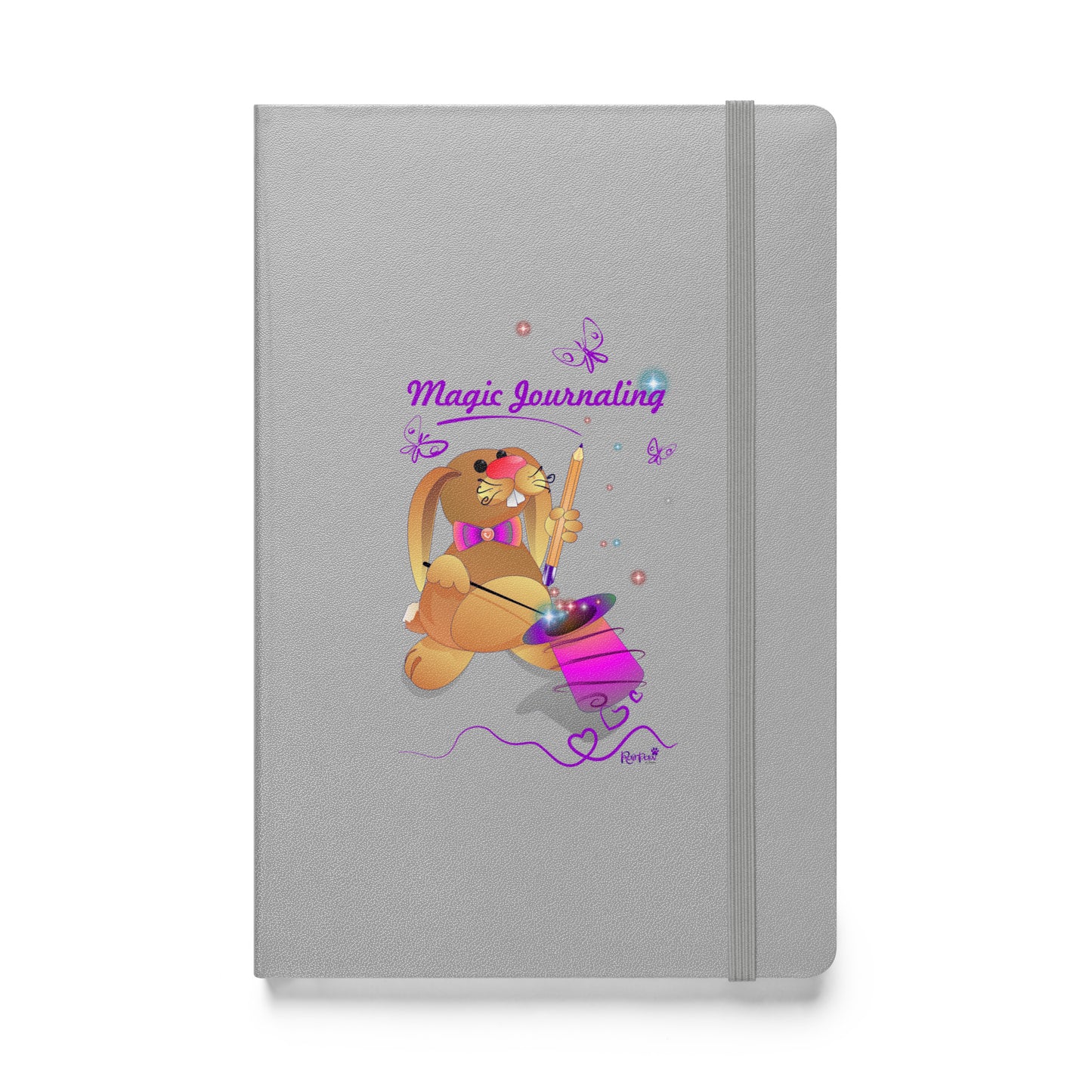 Silver notebook on a white background.  A rubber band wraps around the opening edge of the journal to keep it closed.  - The cover features a bunny holding a magic wand and a pencil pulled from its top hat, surrounded by butterflies, colourful stars, and hearts, giving the journal an enchanting feel. The words "Magic Journaling" are written on the cover.