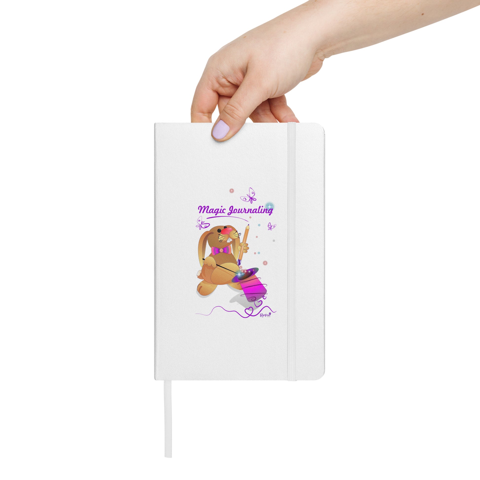 White notebook held by a hand on a white background. - The cover features a bunny holding a magic wand and a pencil pulled from its top hat, surrounded by butterflies, colourful stars, and hearts, giving the journal an enchanting feel. The words "Magic Journaling" are written on the cover.