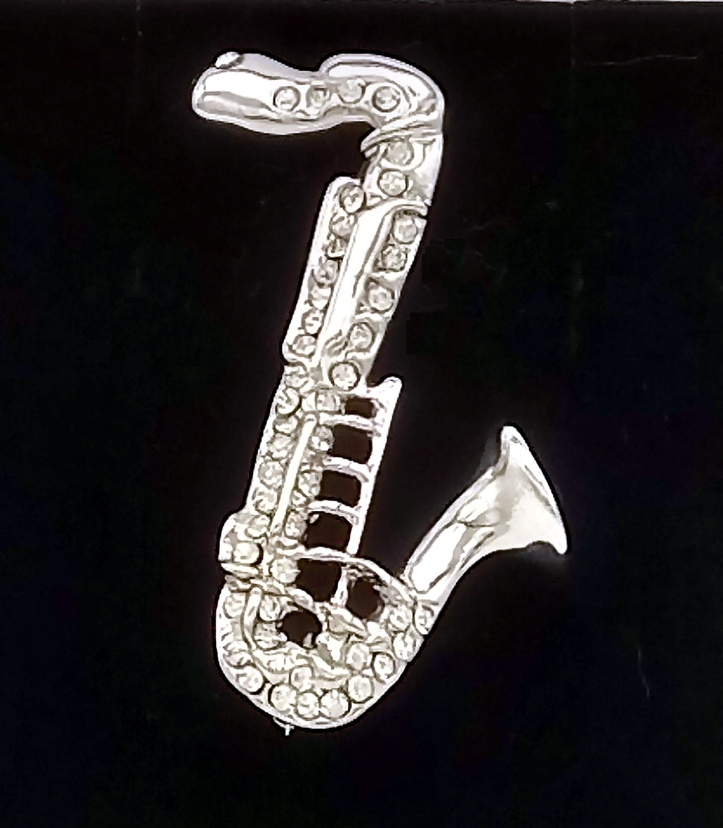 Silver saxophone-shaped brooch with rhinestones on a black background