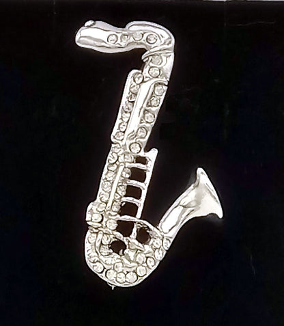 Silver saxophone-shaped brooch with rhinestones on a black background