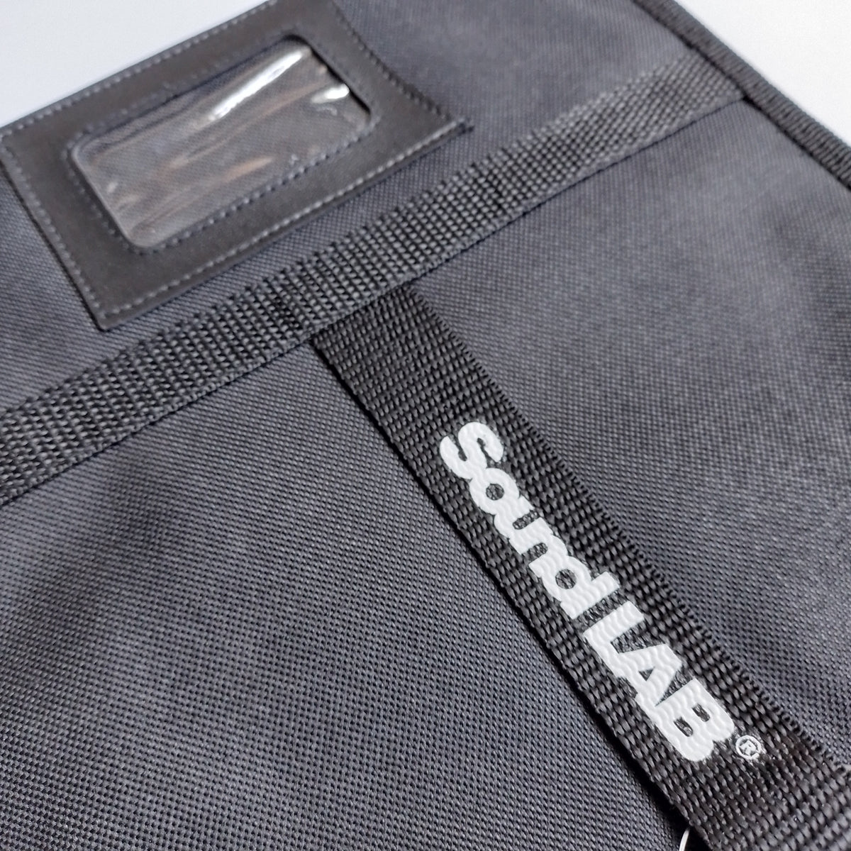 Close-up of black pouch or organizer with a clear ID window and a black webbed strap featuring the white 'Sound LAB' logo. 