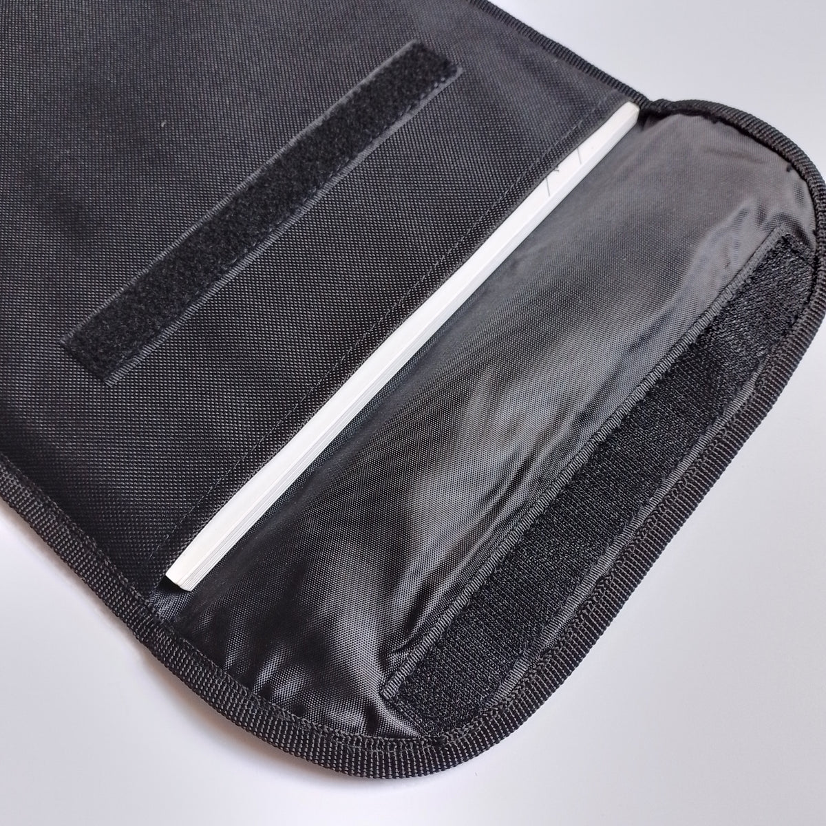 Close-up of a black fabric sleeve or pouch with a hook-and-loop closure and a white interior lining, shown on a light gray background.