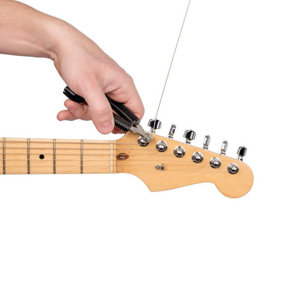 Hand using a tool to cut off excess string off a guitar machine head 