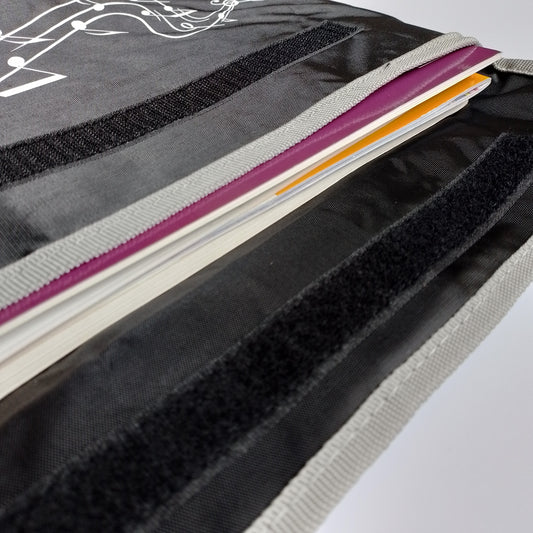 Close-up of a black fabric organizer pouch with hook-and-loop closures, showing a stack of colourful books, sheets or folders inside a bag.