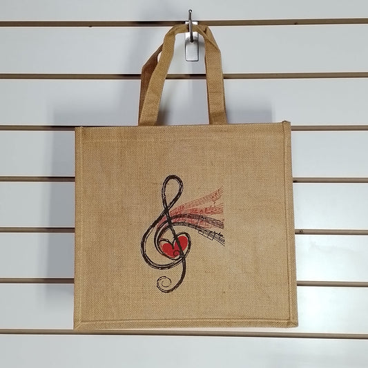 A natural jute tote bag with a treble clef and red heart graphic, hanging from a metal hook on a white slatwall.