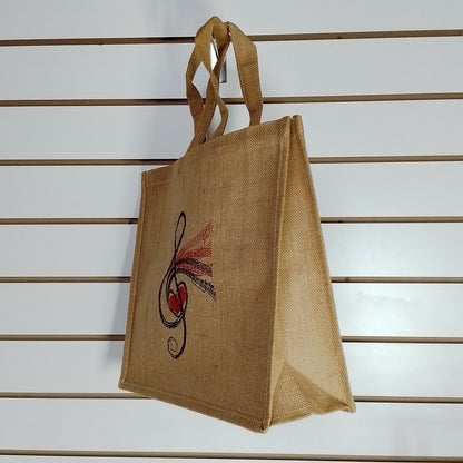 A natural jute tote bag hanging on a white slatwall, featuring a black and red printed musical note and heart design on the front.