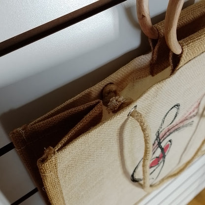 A close-up of a beige burlap tote bag with natural wood handles, hanging against a white wall.