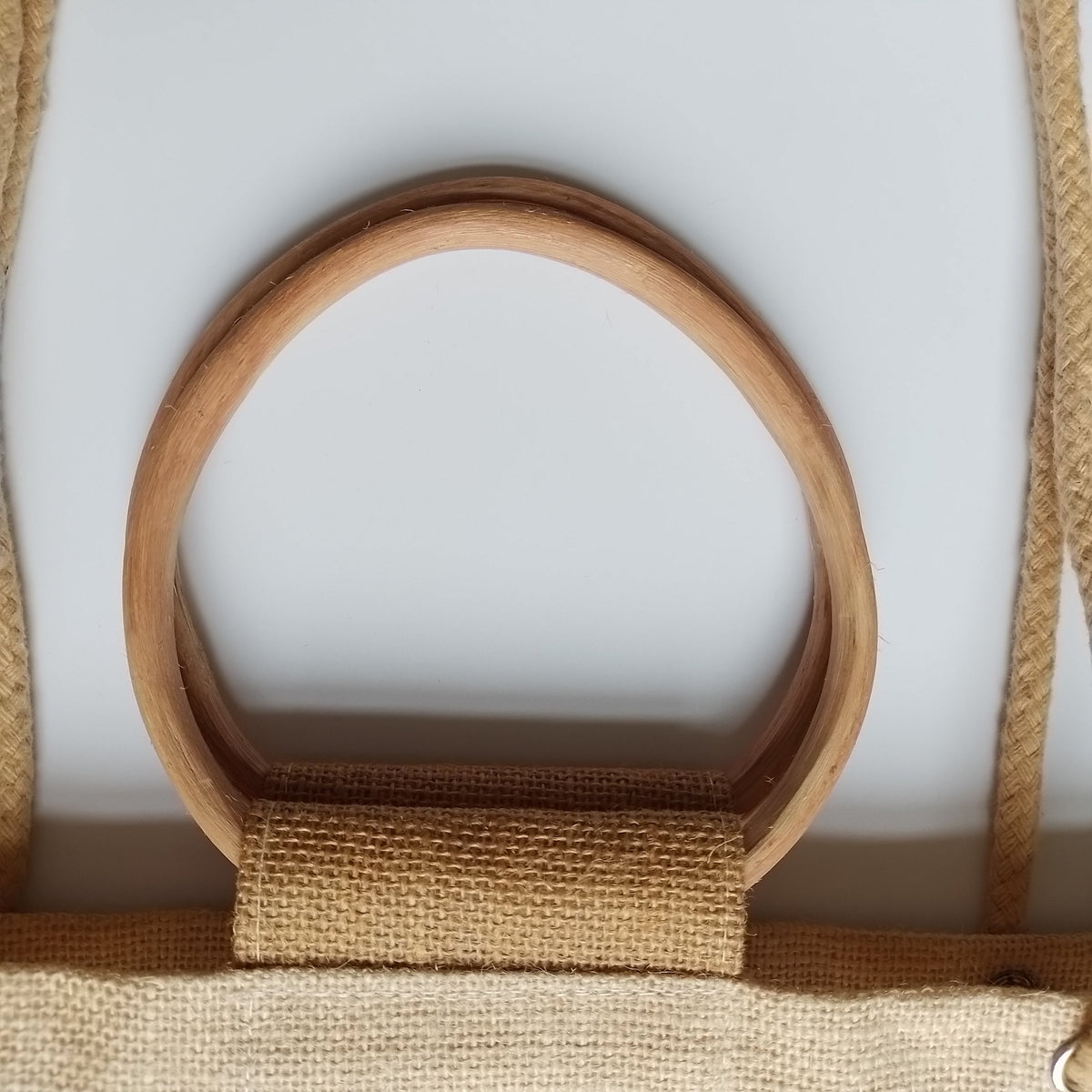 Close-up of a natural wood oval ring handle attached to a tan burlap or jute fabric strap on a light gray background.