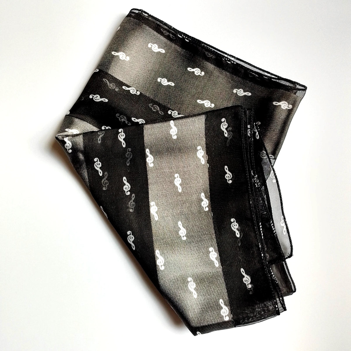 A black sheer scarf with white treble clef patterns, folded neatly on a white background.