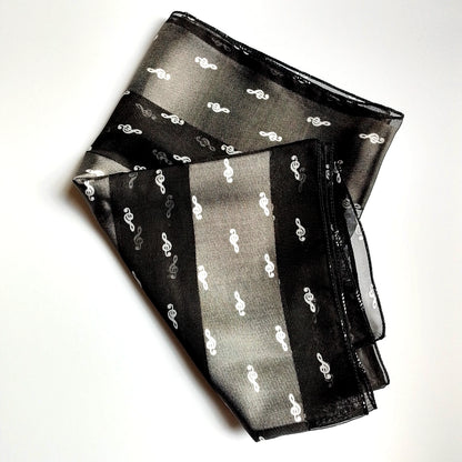 A black sheer scarf with white treble clef patterns, folded neatly on a white background.
