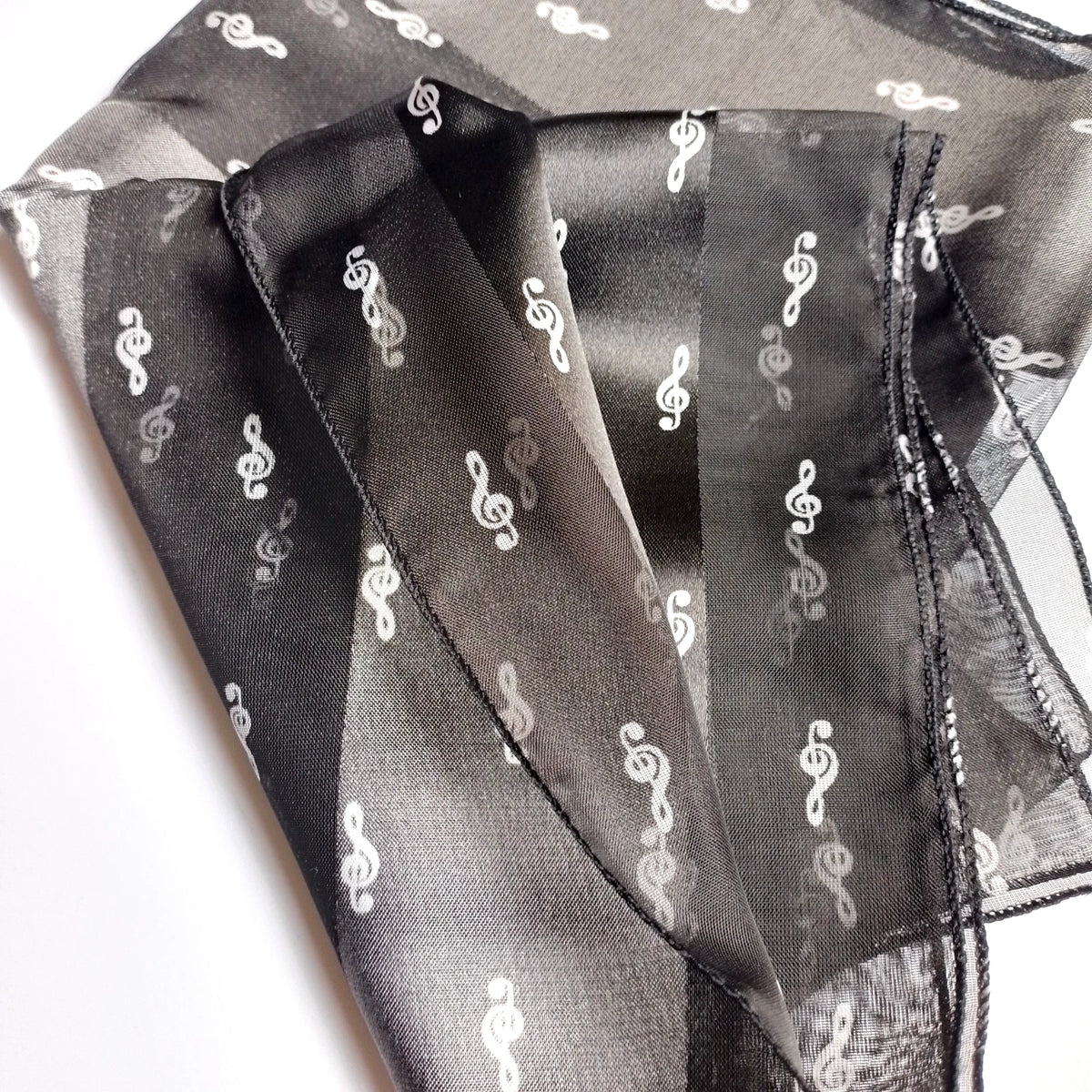 A sheer black organza scarf with a repeating white treble clef pattern, folded to show its texture and semi-transparent quality.