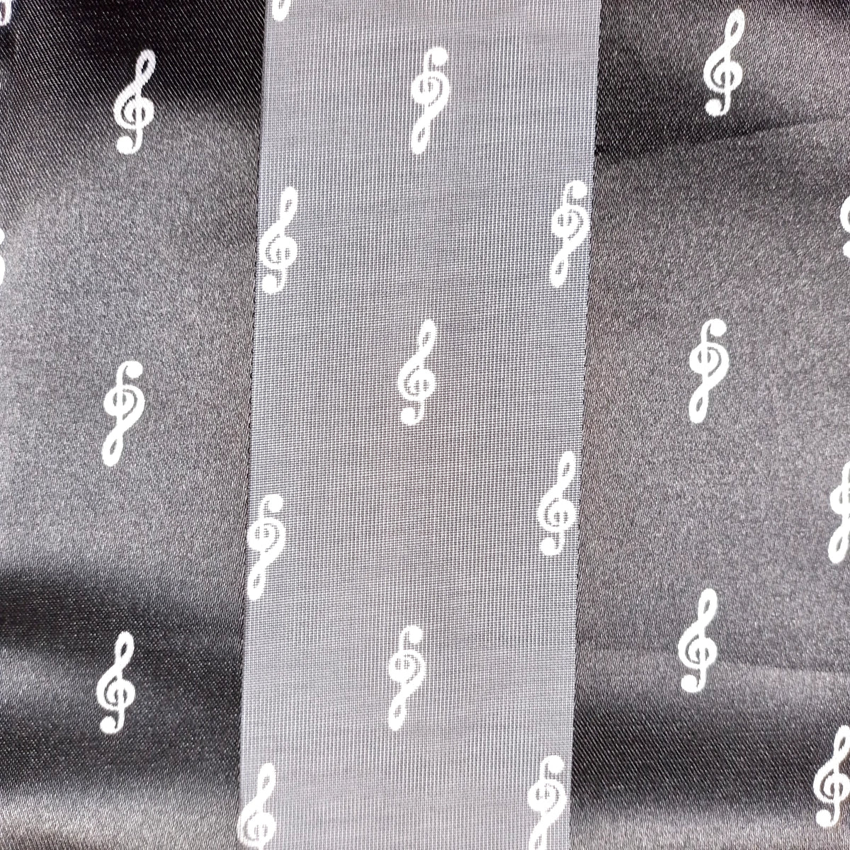 A close-up of a black fabric with a repeating white treble clef pattern, shown with a vertical fold in the centre.