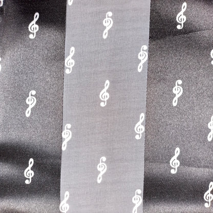 A close-up of a black fabric with a repeating white treble clef pattern, shown with a vertical fold in the centre.