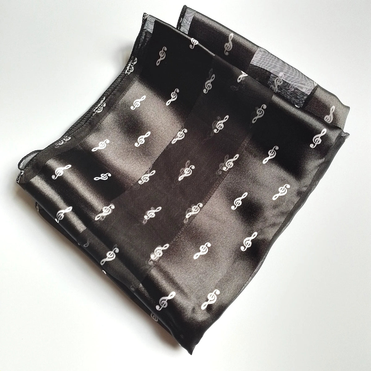 A folded black satin pocket square featuring a repeating pattern of small white treble clef, displayed on a clean white background.
