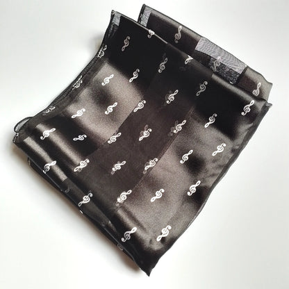 A folded black satin pocket square featuring a repeating pattern of small white treble clef, displayed on a clean white background.