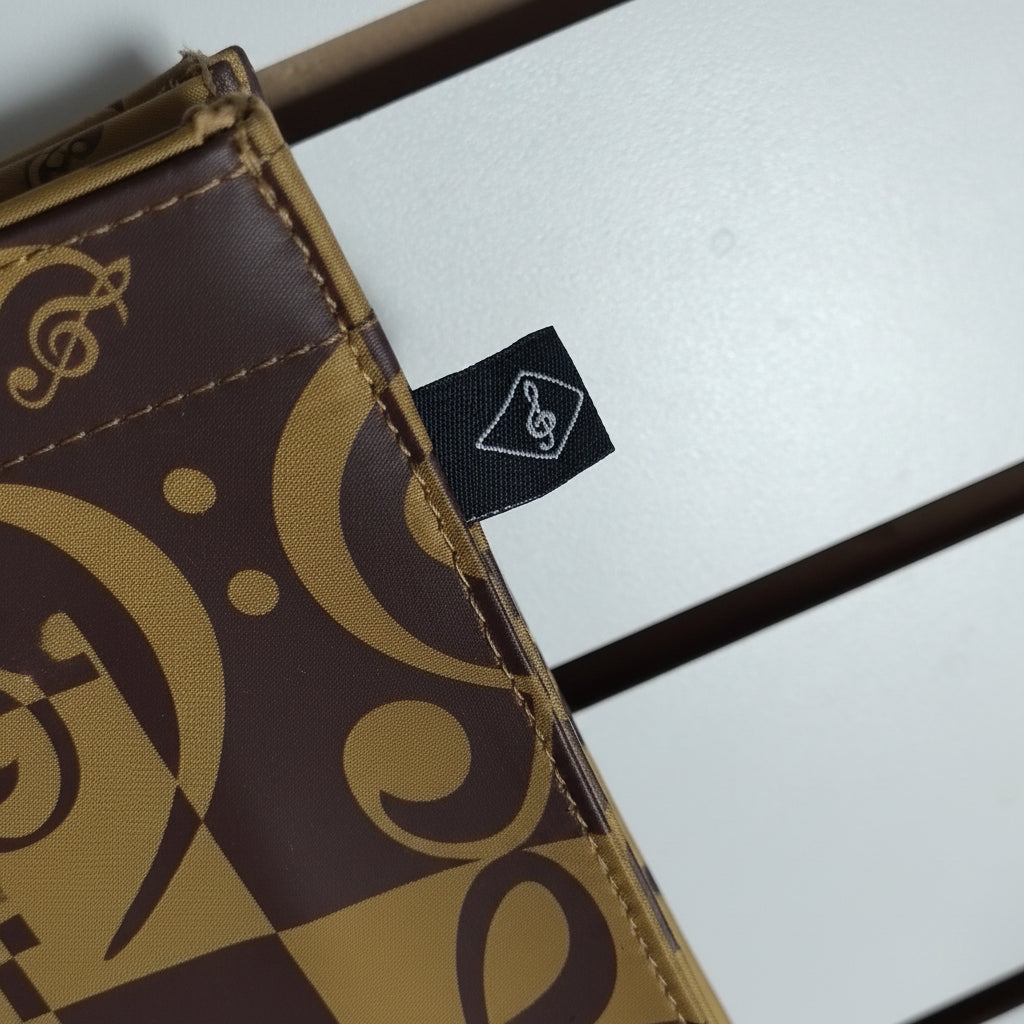 Close-up of a brown and tan patterned wallet or card case with a small black fabric tag featuring a white logo, set against a light gray background with dark horizontal bars.