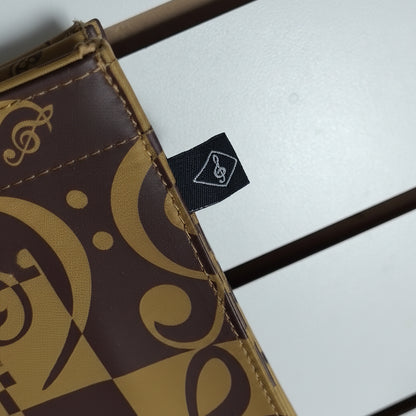 Close-up of a brown and tan patterned wallet or card case with a small black fabric tag featuring a white logo, set against a light gray background with dark horizontal bars.