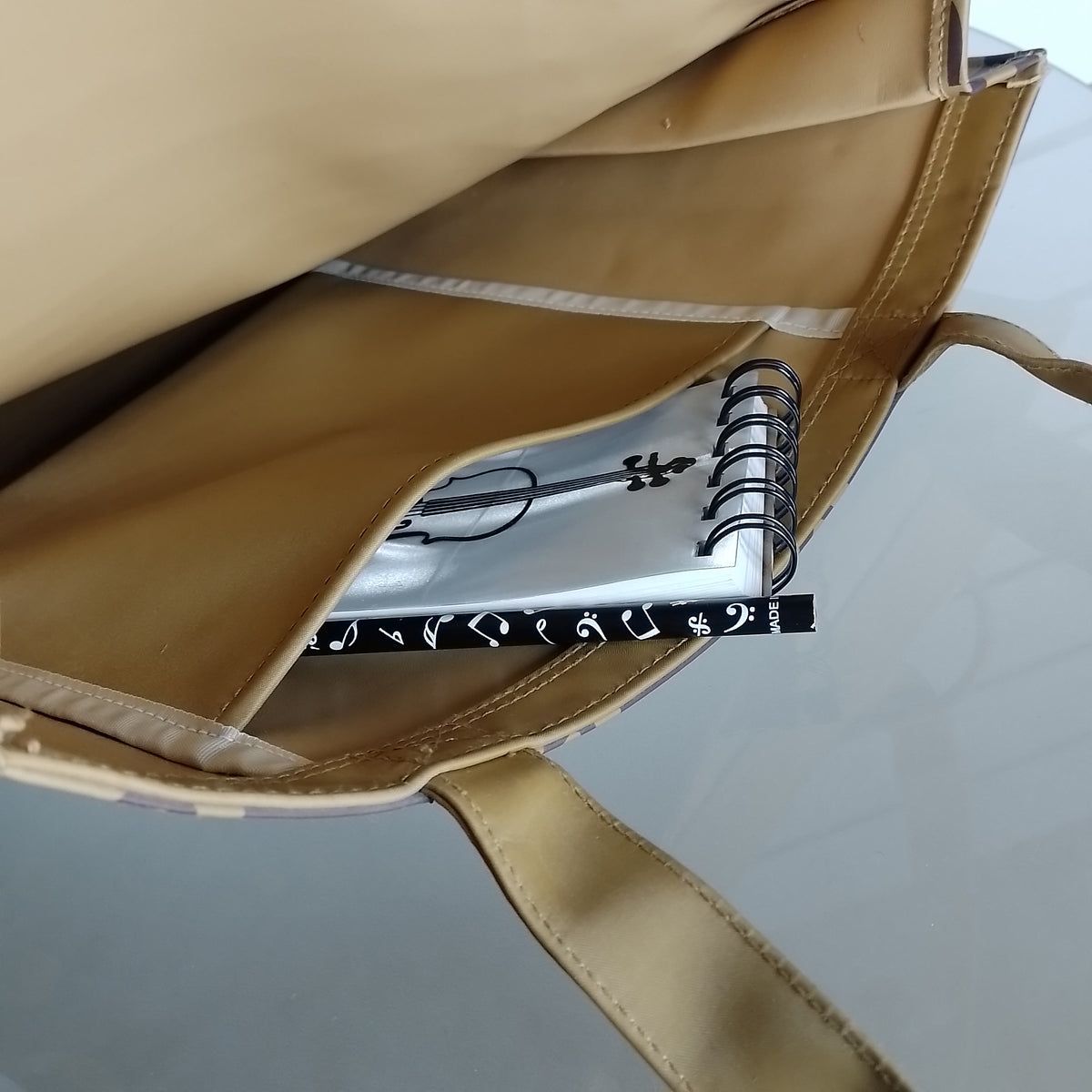 Close-up of a beige tote bag opening, showing a white spiral notebook tucked inside a side pocket.