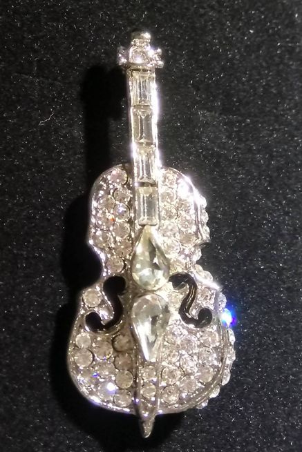 Decorative brooch shaped like a violin with gemstones on a black background