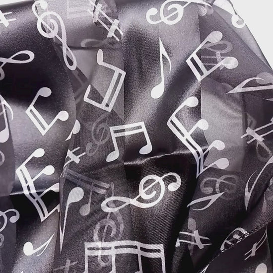 A lightweight black scarf with a white musical note pattern, styled in a loose knot on a plain white surface.