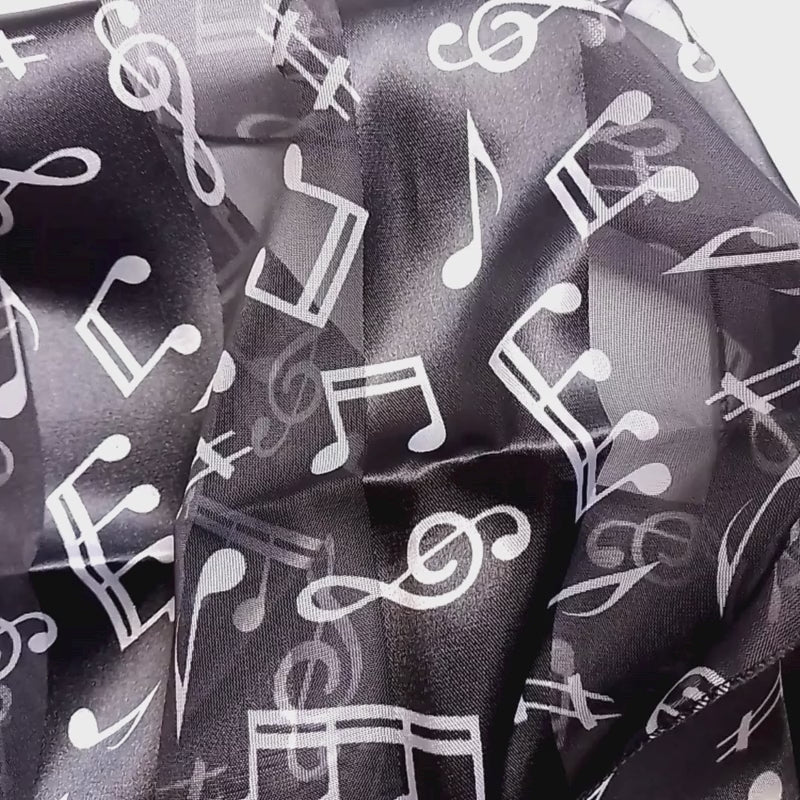 A lightweight black scarf with a white musical note pattern, styled in a loose knot on a plain white surface.