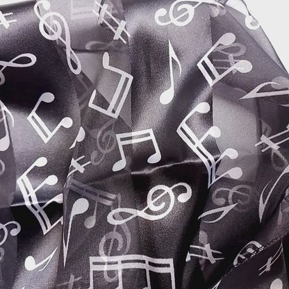 A lightweight black scarf with a white musical note pattern, styled in a loose knot on a plain white surface.