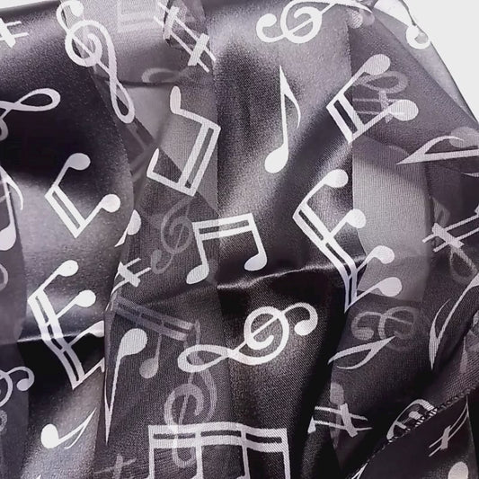 A lightweight black scarf with a white musical note pattern, styled in a loose knot on a plain white surface.
