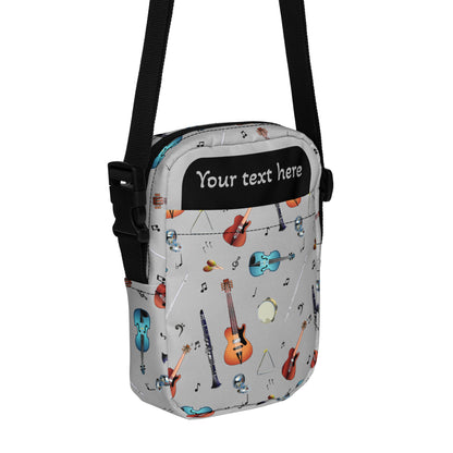 Grey crossbody bag with black adjustable shoulder strap (with black plastic clip), inside and outside pockets, sturdy fabric, and two-way zipper. The design features a repeat pattern of colourful musical instruments and black musical notes on a grey background.