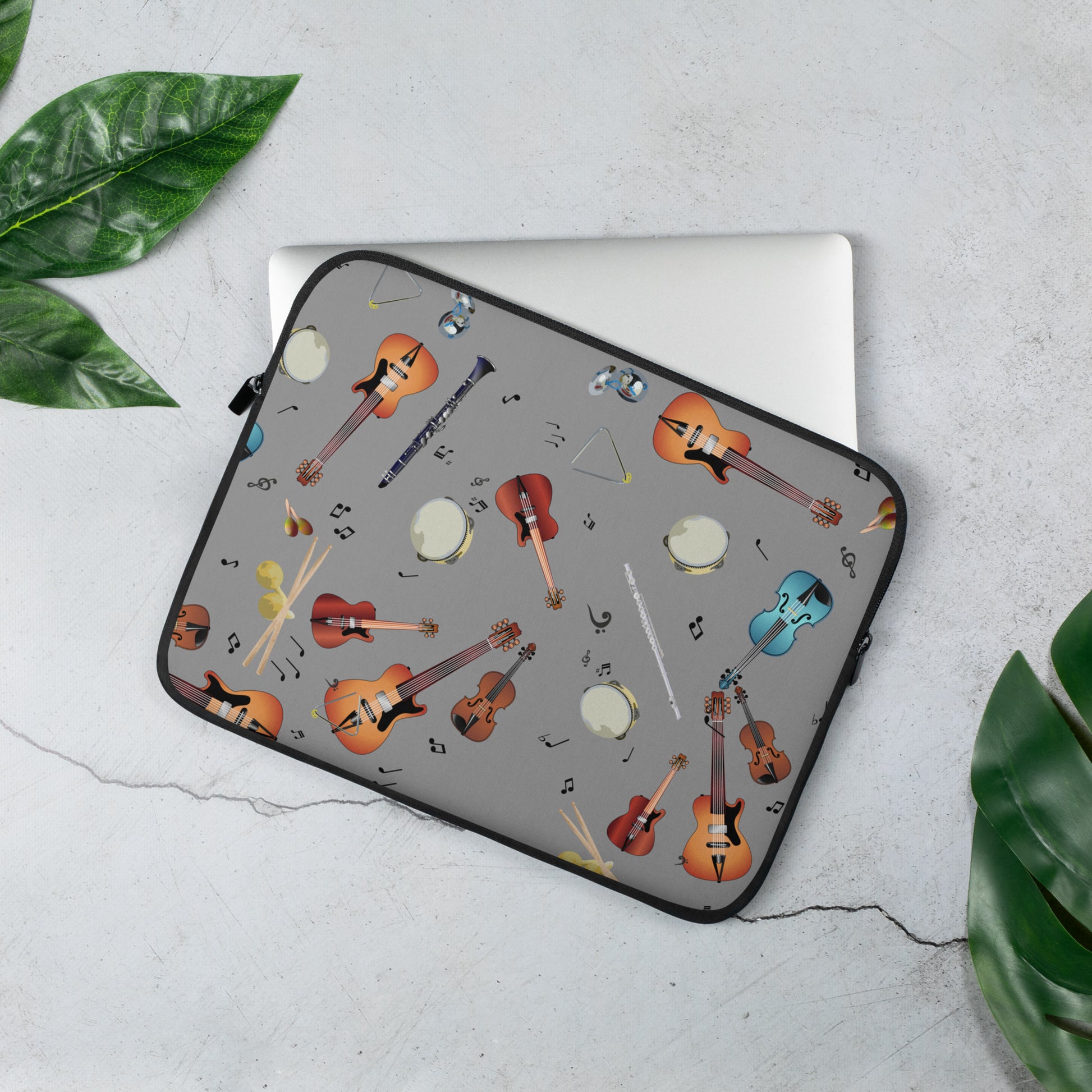 Laptop sleeve with musical instrument pattern on a light gray surface with green leaves.